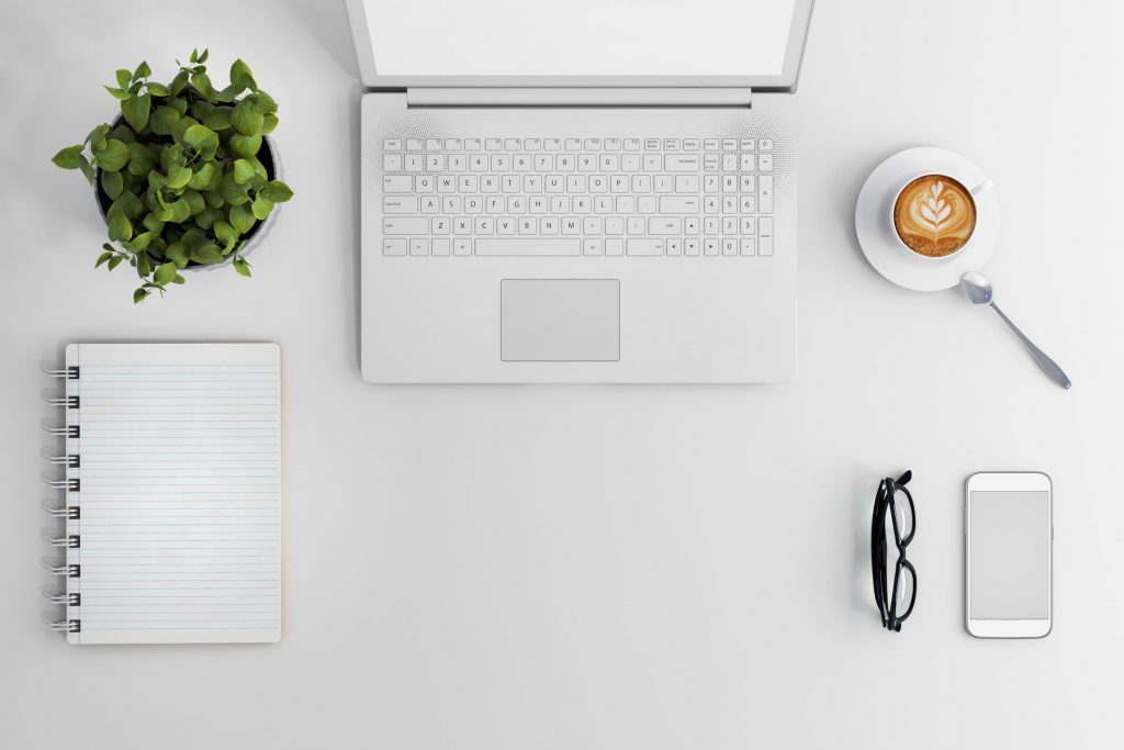 A laptop, plant, notebook, coffee and phone on a desk