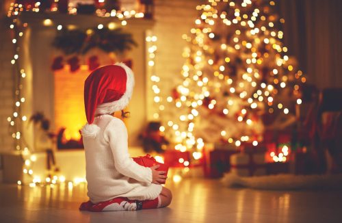 Child wearing Santa hat staring at a lit Christmas tree