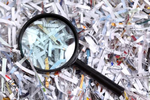 Pile of shredded documents with a magnifying glass sitting on top