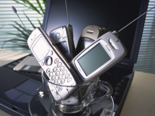 Four cell phones sitting in a glass cup